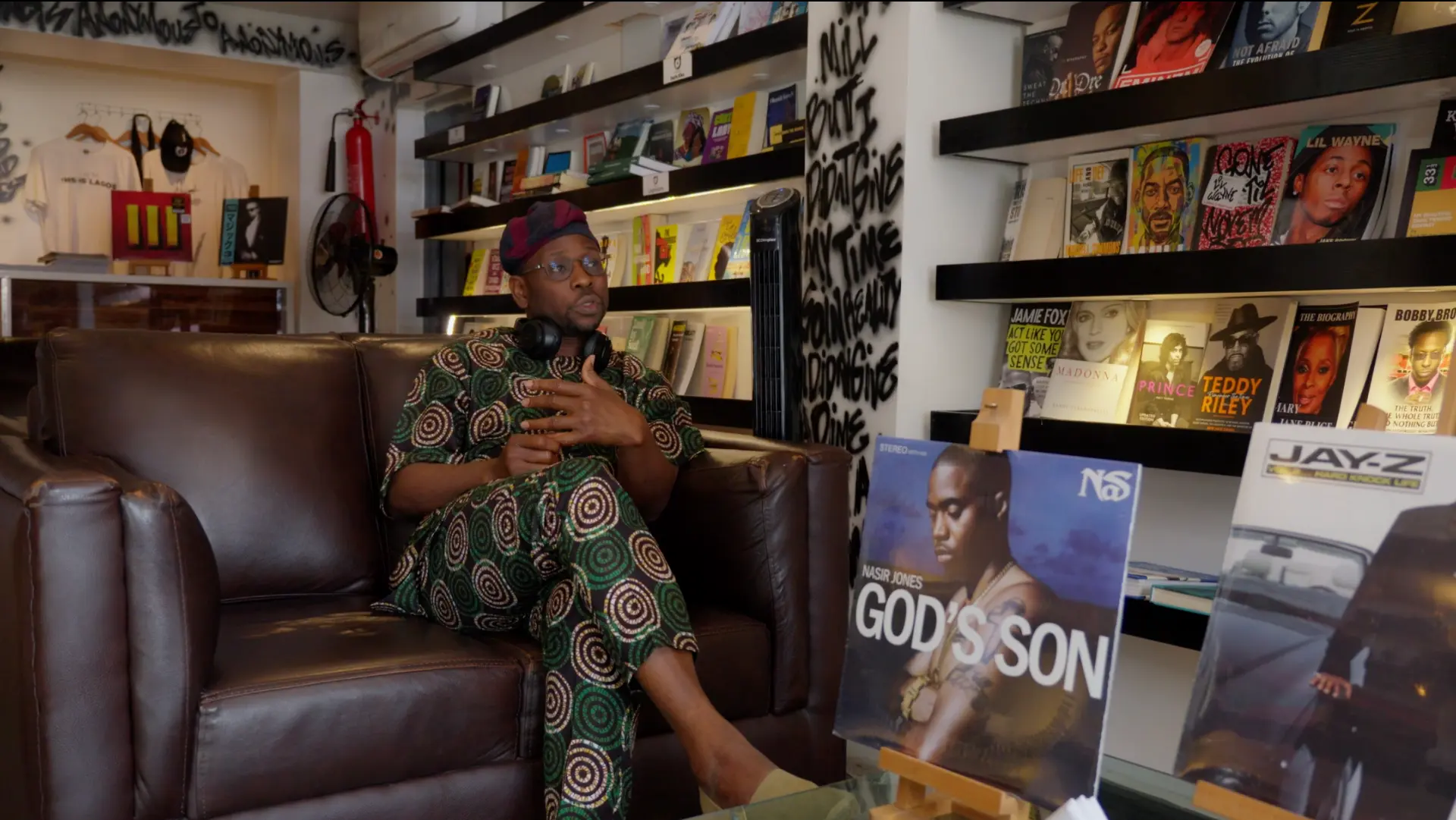A man in patterned attire speaking on a leather sofa in a record and book store